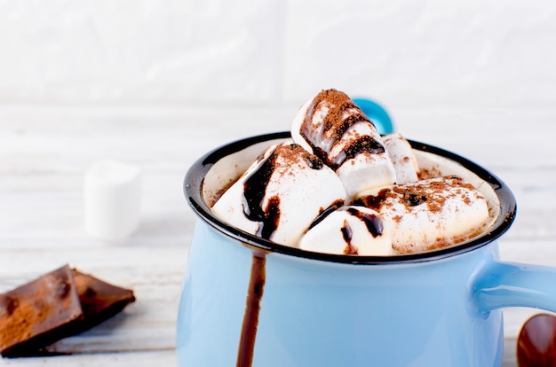 Cacao à la guimauve et au chocolat dans une tasse bleue sur le fond en bois ancien