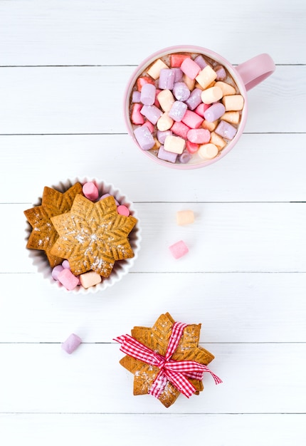 Cacao de Noël avec guimauve dans une tasse rose et un biscuit au gingembre sur une table en bois