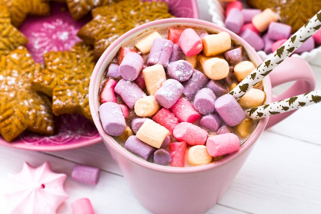 Cacao de Noël avec guimauve dans une tasse rose et un biscuit au gingembre sur une table en bois