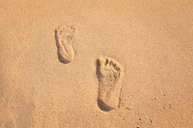 cachet de pieds sur le sable sur la plage avec le soleil dans la matinée