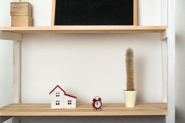 Cactus, maison modèle et réveil rétro sur étagère en bois. Décoration intérieure aux couleurs claires.