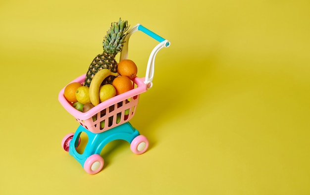 Caddie rose pour enfants jouet plein de fruits exotiques assortis isolés sur jaune avec espace de copie. Vue grand angle