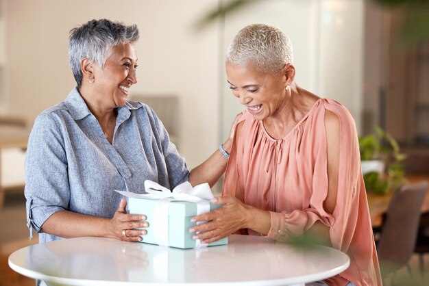 Cadeau d'amis et heureux avec les femmes et la boîte pour la fête de Noël et la surprise d'anniversaire à la maison Vacances actuelles et festives avec une dame âgée à table pour les félicitations et la tradition