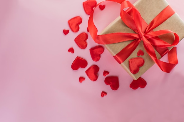 Cadeau artisanal noué avec un ruban rouge avec des coeurs sur fond rose Saint Valentin