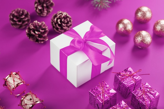 Cadeau dans une boîte blanche et décorations pour arbres de Noël sur un mur rose. Concept rose de décorations de Noël