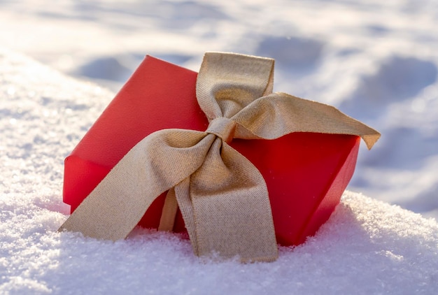 Photo un cadeau dans une boîte rouge avec un arc doré se trouve sur la neige le concept du nouvel an noël félicitations de la saint-valentin en hiver