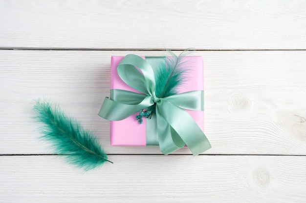 Un cadeau dans un emballage rose et une plume sur un fond en bois blanc.