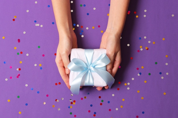 Cadeau dans les mains des femmes sur un fond coloré avec vue de dessus de confettis