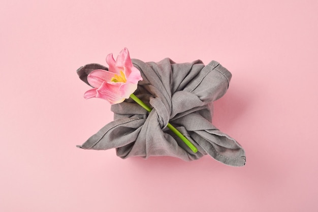 Cadeau écologique printanier emballé dans du textile gris avec une fleur de tulipe rose