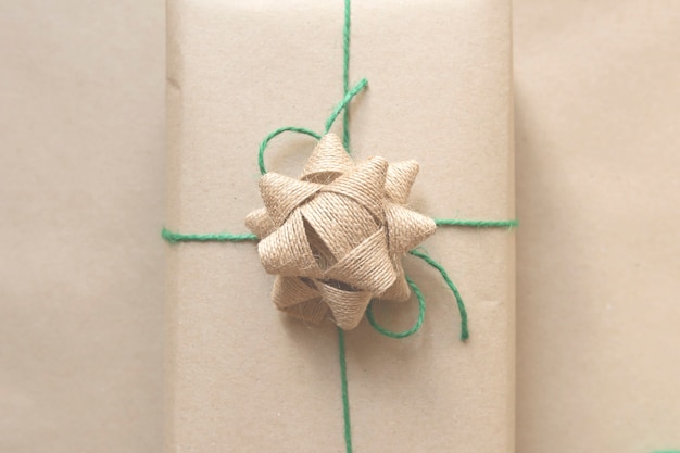 cadeau emballé dans du papier recyclé uni avec ruban de toile de jute et fil vert sur fond beige