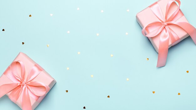 Cadeau emballé rose ou coffret cadeau rose pastel avec archet sur fond bleu pastel avec des confettis de coeurs, espace de copie, vue de dessus, mise à plat. Contexte pour la Saint-Valentin, la fête des mères ou un anniversaire
