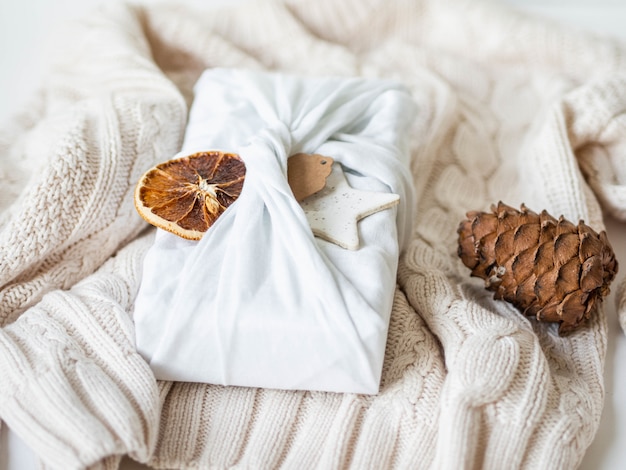 Cadeau enveloppé de tissu avec étiquette en papier, tranche d'orange sèche et étoile en céramique. Alternative réutilisable et durable d'emballage cadeau.