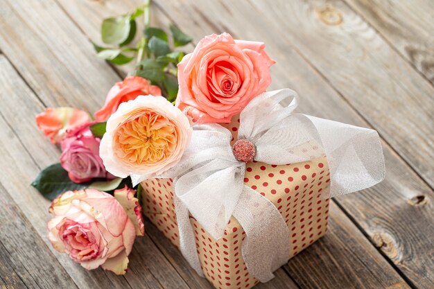 Cadeau joliment emballé et un bouquet de roses sur un fond en bois flou.