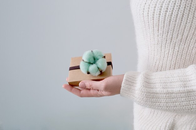 Le cadeau en mains féminines est décoré d'une fleur de coton turquoise.