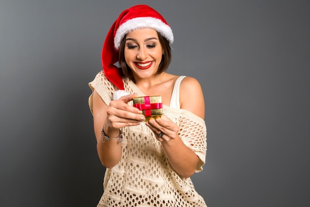 Cadeau de Noël - cadeau d'ouverture femme surpris et heureux, jeune belle femme souriante en bonnet de Noel.