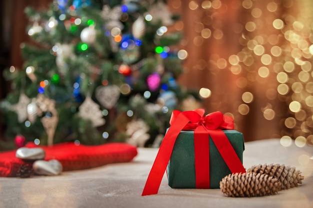 Cadeau de Noël dans une boîte verte avec un arc rouge sur fond d'arbre de Noël.