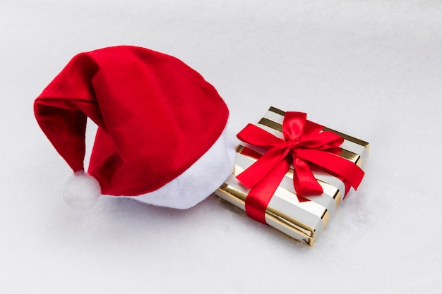 Photo cadeau de noël dans un emballage festif et un chapeau de père noël sur la neige.