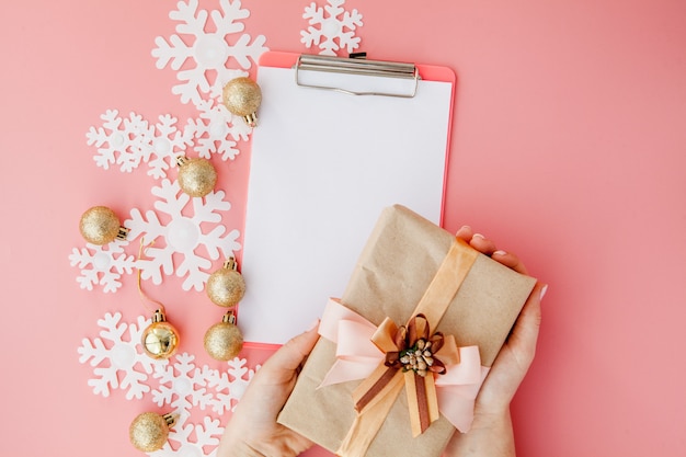 Cadeau de Noël dans les mains des femmes et cahier sur fond rose