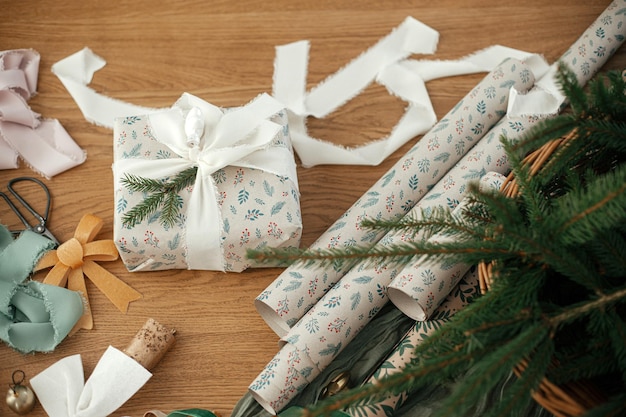 Cadeau de Noël élégant avec un nœud blanc et des rubans festifs ciseaux cloches et décorations modernes sur une table en bois vue joyeux Noël et joyeuses vacances