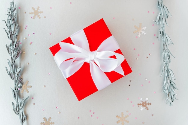Cadeau de Noël avec noeud de ruban et brindilles décoratives en argent, paillettes et paillettes de flocon de neige. Mise à plat