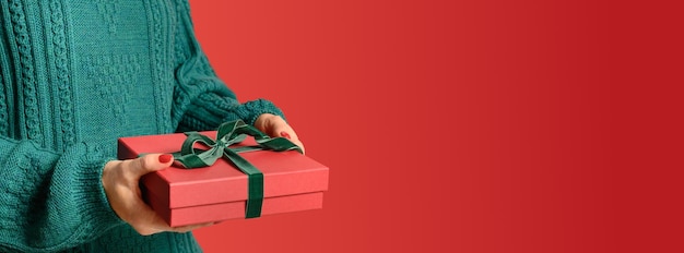 Cadeau de Noël rouge dans les mains de la femme dans la bannière de Noël pull vert chaud