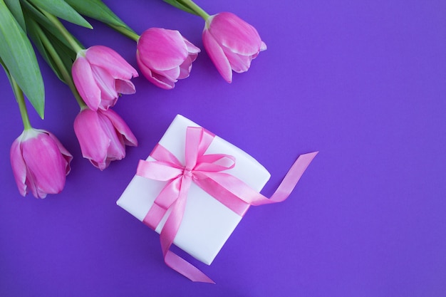 Cadeau avec noeud rose et tulipes roses sur violet