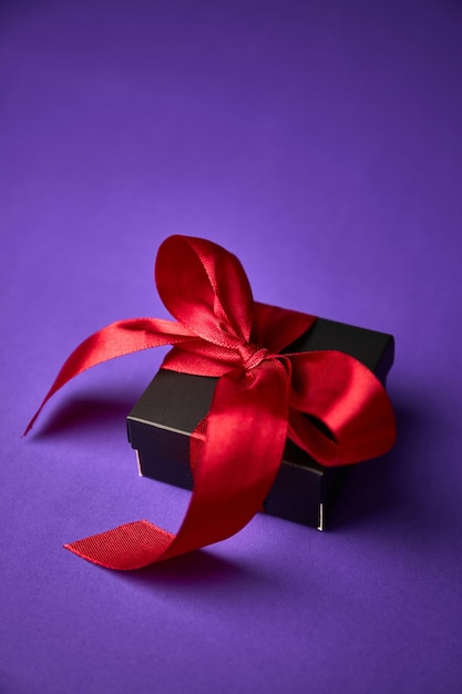 Cadeau noir avec ruban rouge sur fond violet Saint Valentin Anniversaire ou concept de vacances Espace de copie