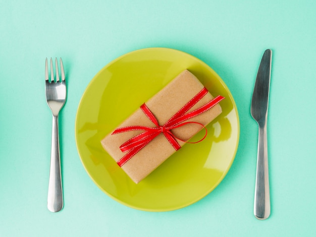 Cadeau, paquet de papier Kraft brun avec ruban rouge sur une assiette jaune, couteau, fourchette. Valentine