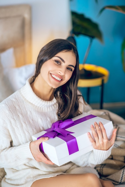 Cadeau d'un petit ami. Femme aux cheveux noirs tenant un cadeau dans ses mains et souriant