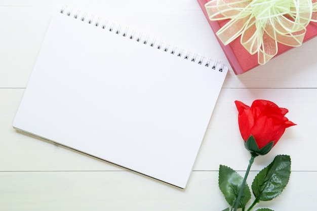 Cadeau présent avec fleur rose rouge et cahier avec espace copie sur une table en bois