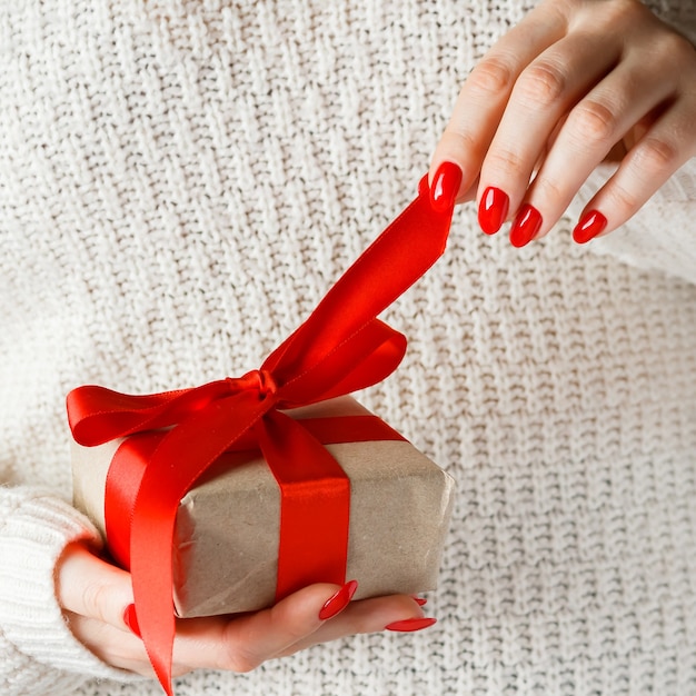 Cadeau avec un ruban rouge en mains sur fond blanc