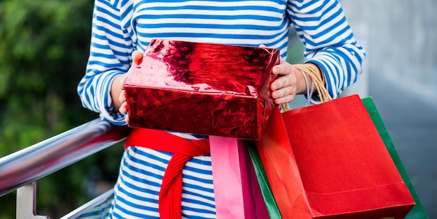 Cadeau de shopping et cadeau le lendemain de Noël pour la fête de Noël et du nouvel an. Jeunes femmes tenant un sac à provisions et une boîte rouge.