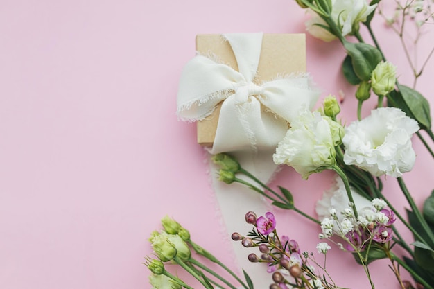 Cadeau simple et élégant avec ruban et belles fleurs tendres sur fond rose à plat avec un espace pour le texte Bonne fête des femmes et concept de fête des mères Carte de voeux florale ou bannière