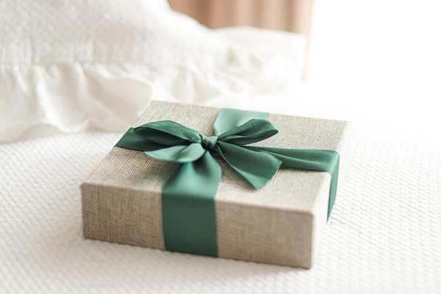 Cadeau de vacances et livraison d'achats en ligne de luxe coffret cadeau en lin enveloppé avec ruban vert sur le lit dans le style campagne chic de la chambre