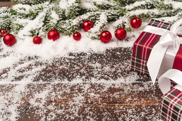 Cadeaux en bois avec des branches de sapin et des boules rouges poudrées de neige