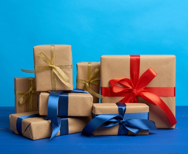 Cadeaux dans des boîtes enveloppées dans du papier kraft brun et attachées avec des rubans de soie sur fond bleu