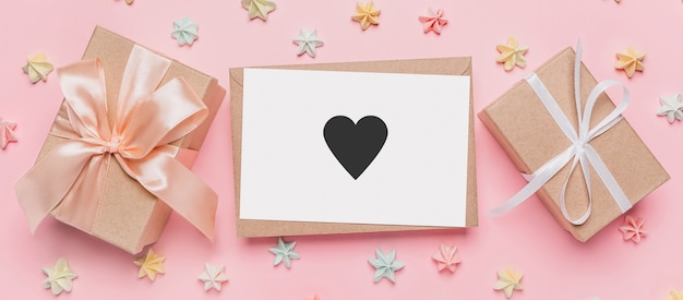 Cadeaux avec lettre de note sur une surface rose isolée avec des bonbons, l'amour et le concept de la Saint-Valentin avec coeur