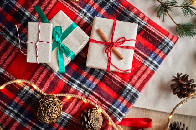 Cadeaux de Noël sur le fond d'un plaid à carreaux en laine rouge avec des guirlandes de cônes et de branches de sapin