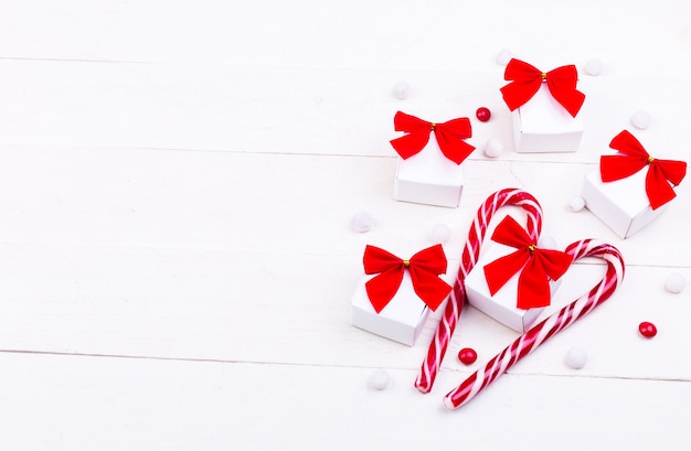 Cadeaux de Noël, petites boîtes blanches avec un arc rouge et des bonbons sur un fond en bois blanc.