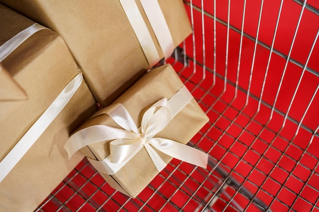 Cadeaux en papier kraft avec du ruban adhésif blanc dans un chariot de supermarché sur fond rouge