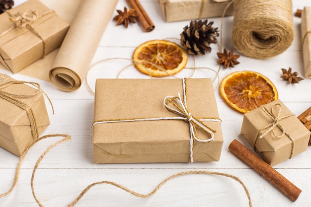 Cadeaux en papier kraft, orange séchée, cannelle, pommes de pin, anis sur une table blanche