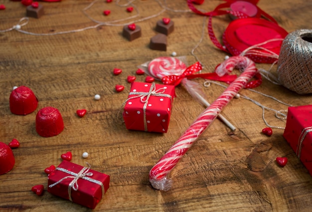 Cadeaux rouges, bonbons, ballons, sucettes, coeurs chocolat sur table en bois. Décoration des roses