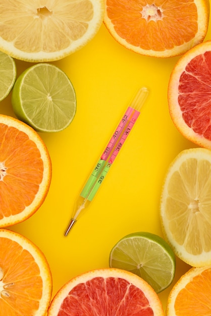 Cadre agrume avec thermomètre au centre. Concept de santé. Fruits antioxydants comme le citron, le citron vert, l'orange et les pamplemousses sur une surface jaune. Mise à plat. Flèche de vitamine.