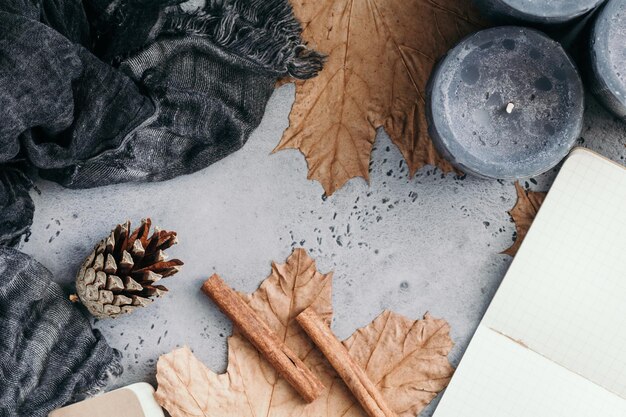Cadre d'automne composition à plat sur fond de béton gris L'érable laisse le cahier ouvert avec des feuilles vides des bougies aromatiques noires et une écharpe chaude
