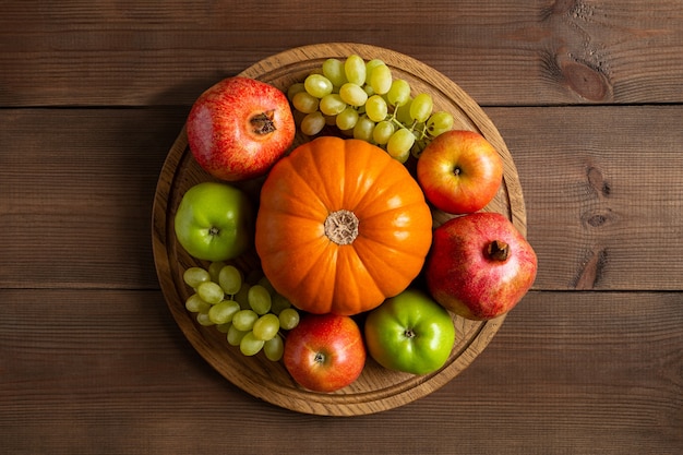 Cadre d'automne nature morte de fruits mûrs citrouille orange, pommes, raisin et grenat. Récolte d'automne sur une planche à découper en bois ronde et fond marron à plat.