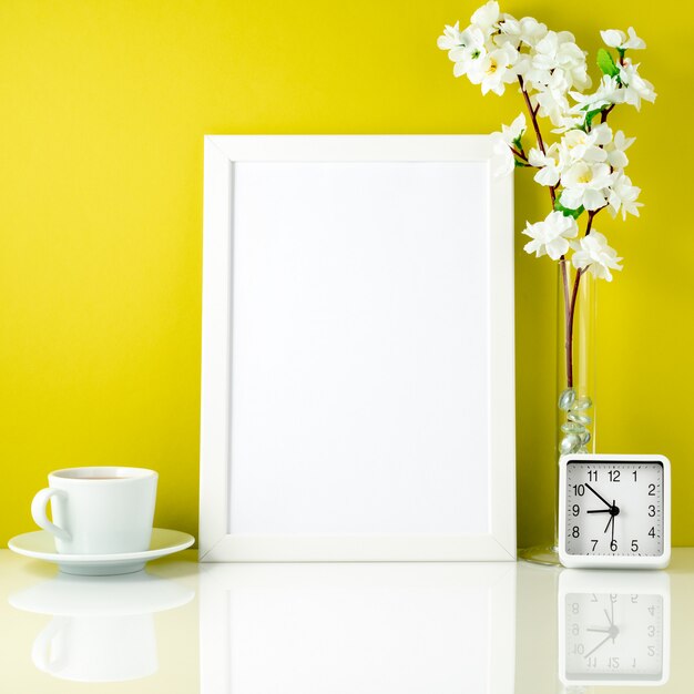 Cadre blanc, fleur dans un vase, tasse de thé ou de café, horloge