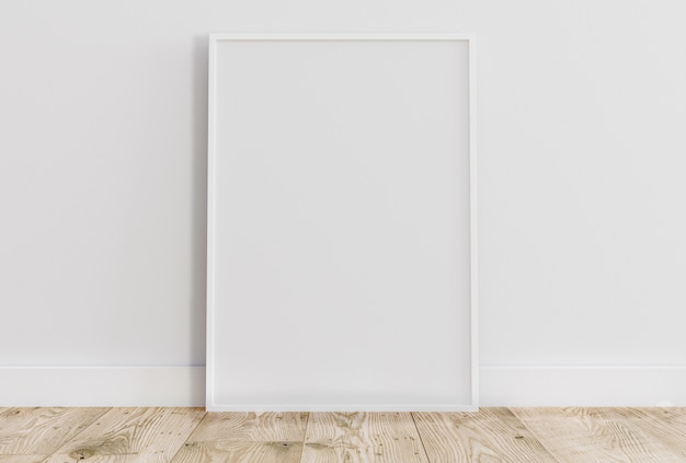 Cadre blanc mince vide sur un plancher en bois clair avec un mur blanc derrière.