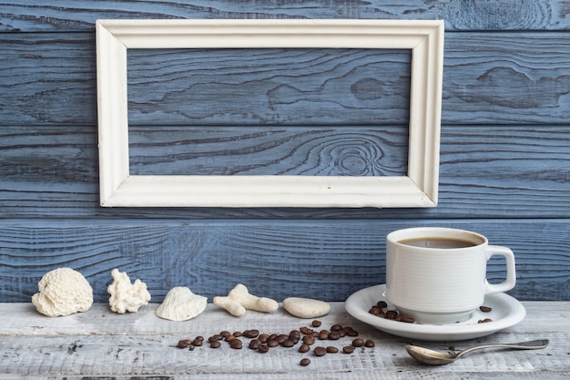 Cadre blanc, tasse à café et coquillages sur fond de planches bleues