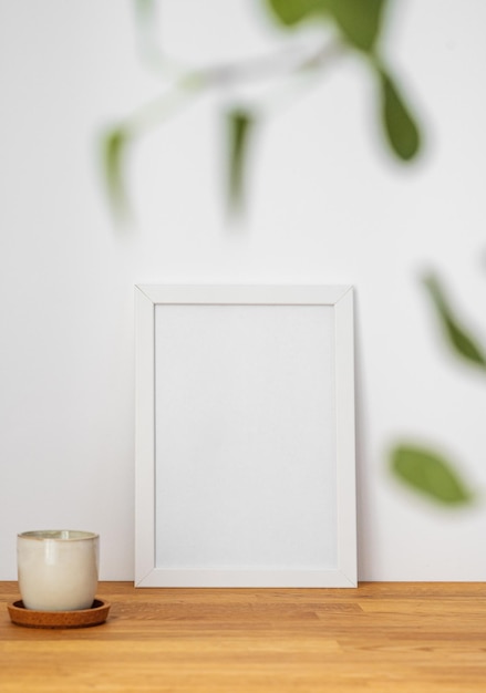Un cadre blanc avec une toile blanche contre un mur léger et sur une table en bois