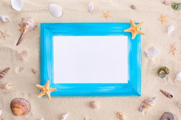 Cadre en bois bleu avec des coquillages blancs et des étoiles de mer sur fond de sable